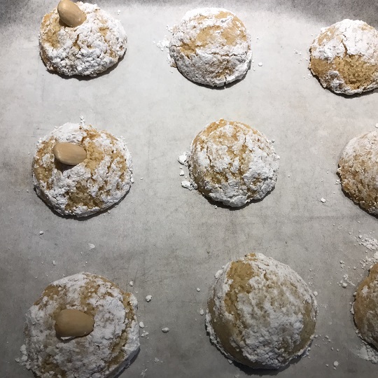 White powder sugar coasted round biscuits on a trey with blanched almonds in centre this is a close up photo of approximately three rows of  biscuits with three lines